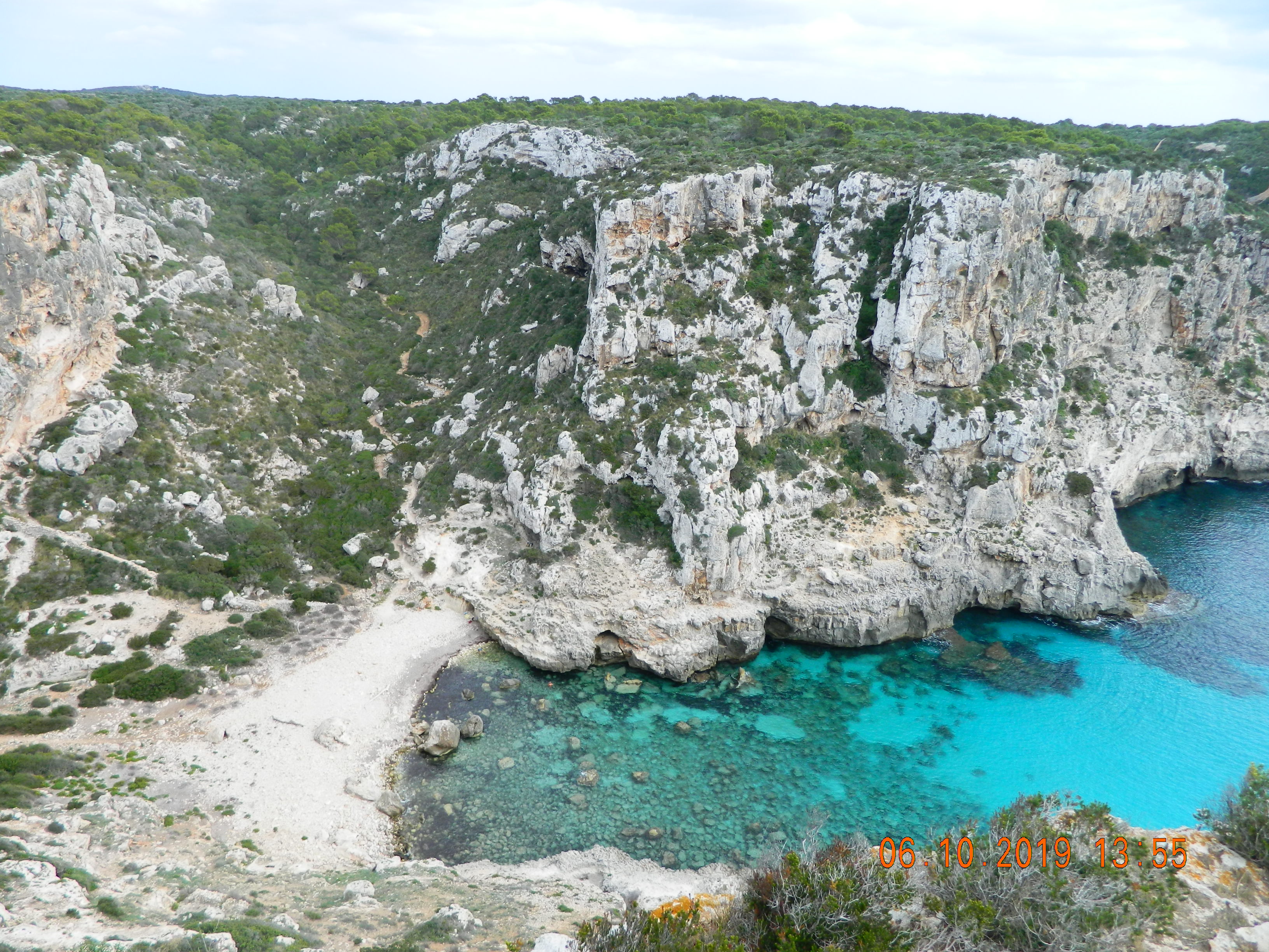 Walking path to Cala Llucalari with pine trees and herbs